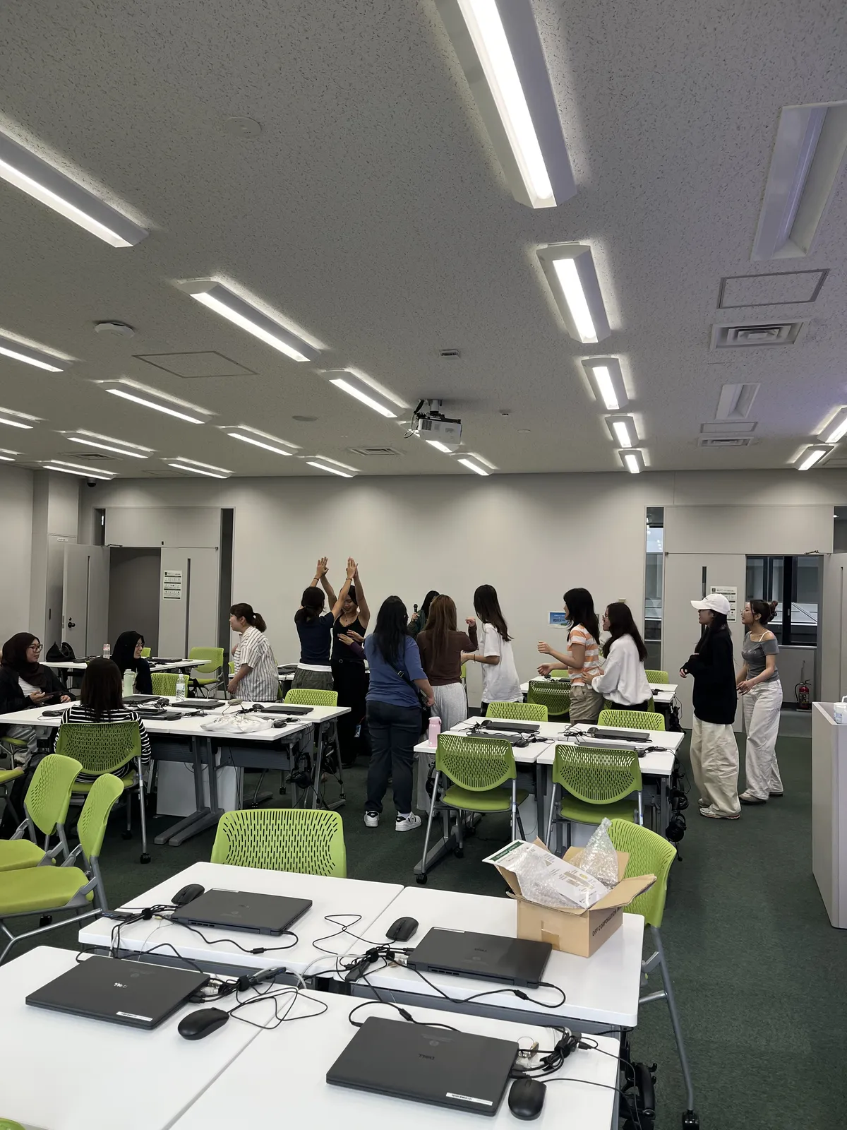 International students standing in the classroom, some pairing up with raised hands to form an arch, trying out a game